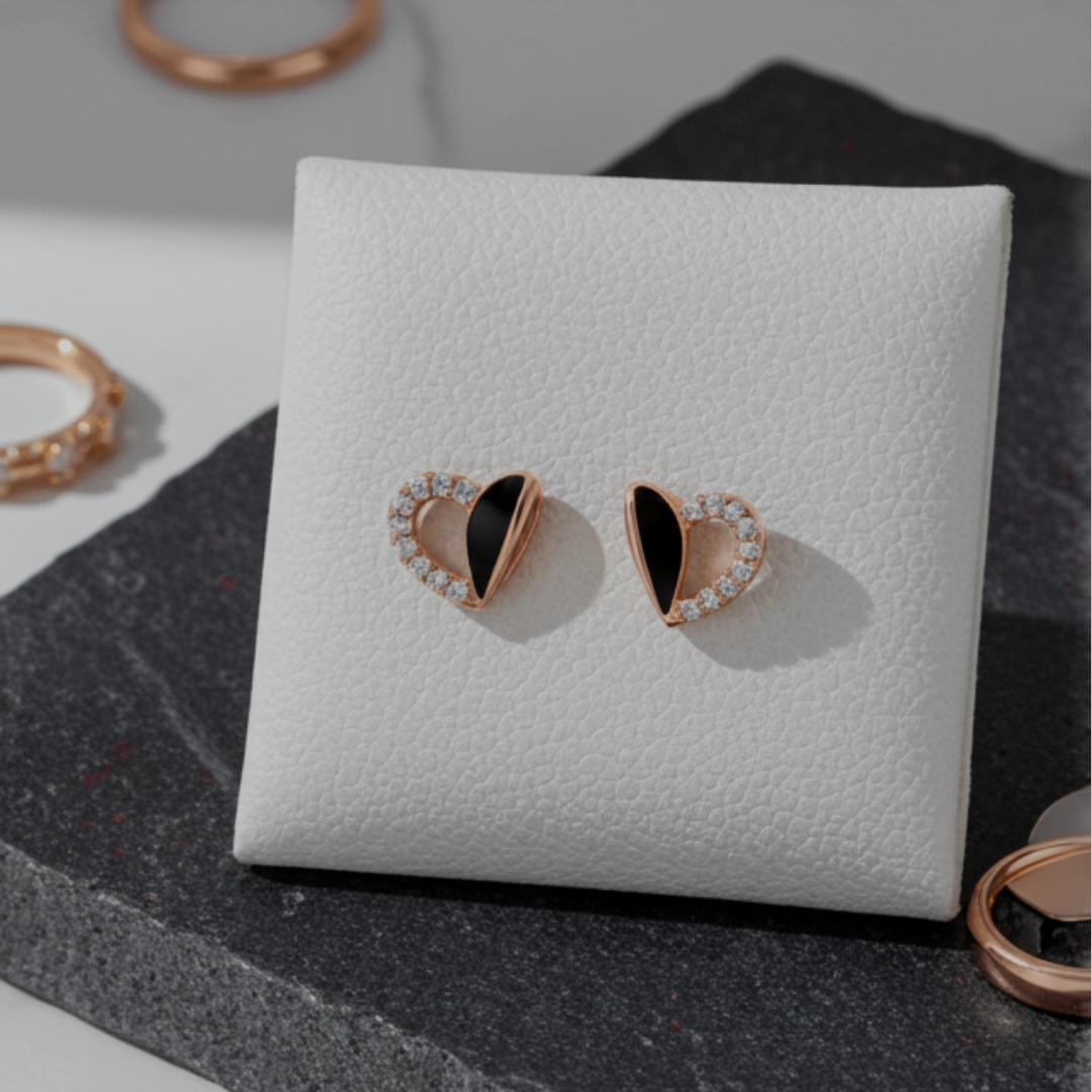 Heart-shaped earrings on a white jewelry display box with rings in the background.